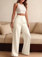 NEWYORKLISTED STYLE COLLECTION: Woman wearing a white sleeveless top and high-waisted pants standing in a living room.