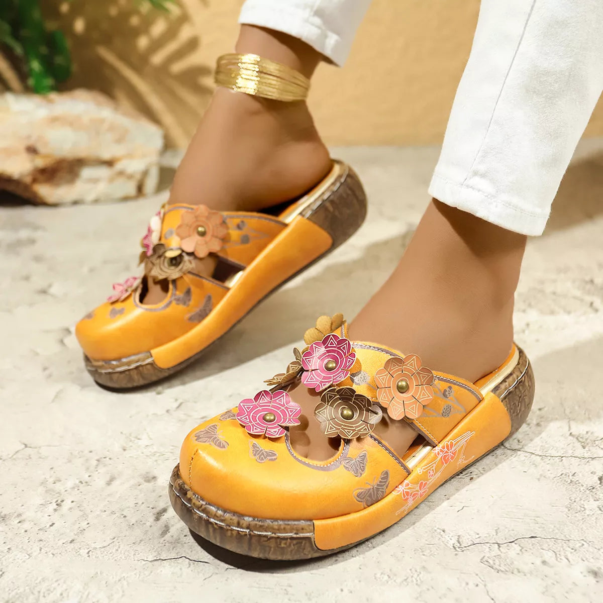 NEWYORKLISTED SHOE COLLECTION: Yellow sandals with floral designs worn by a person on a stone surface.
