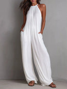 NEWYORKLISTED STYLE COLLECTION: Woman wearing a white halter neck jumpsuit against a gray background