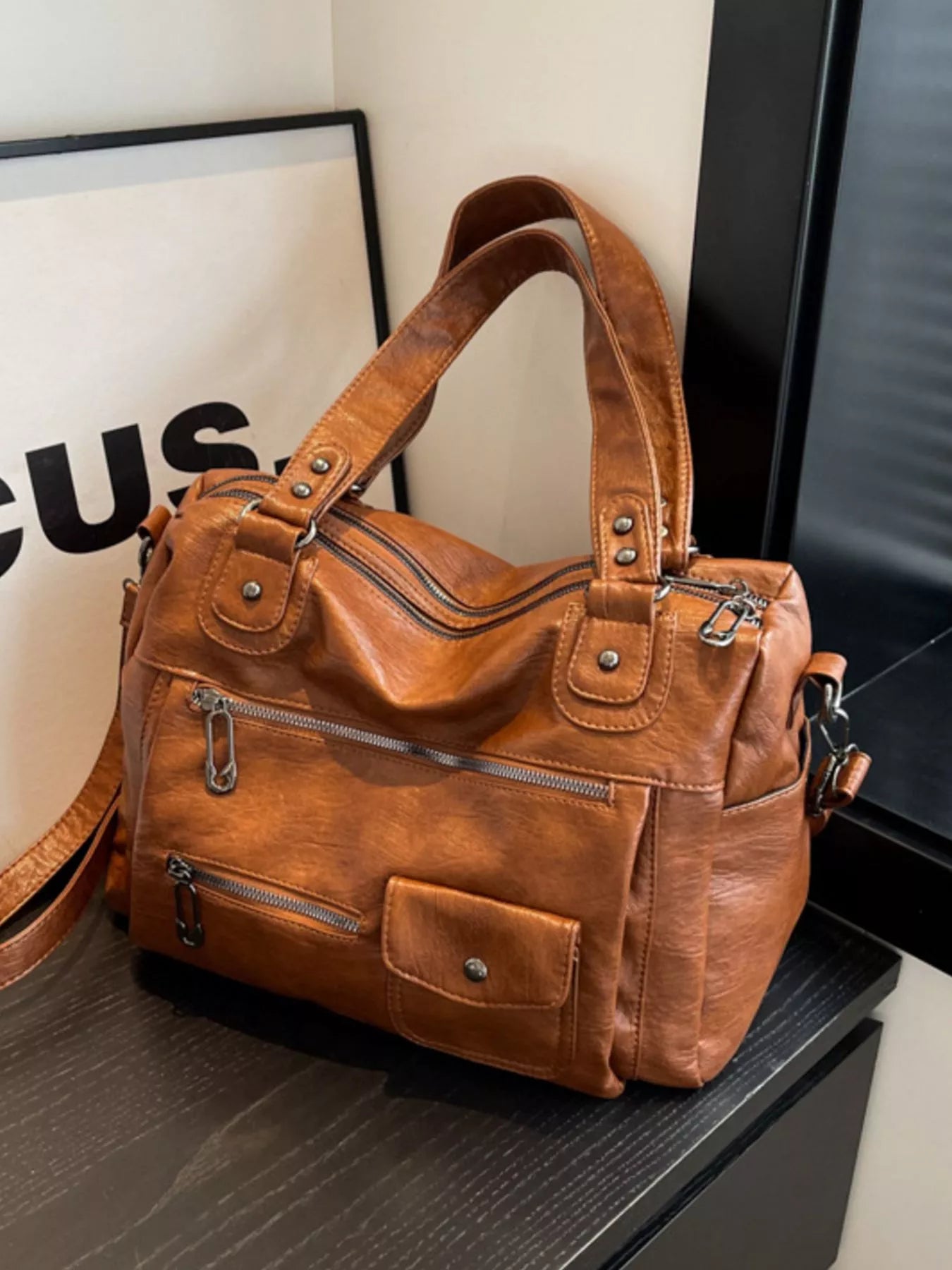 NEWYORKLISTED STYLE COLLECTION: Brown leather handbag on a dark surface with a blurred background