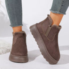NEWYORKLISTED SHOE COLLECTION: A pair of women's brown suede-like ankle boots with plush faux-fur lining and elastic side panels, shown worn with gray frayed-hem jeans on a white studio background.