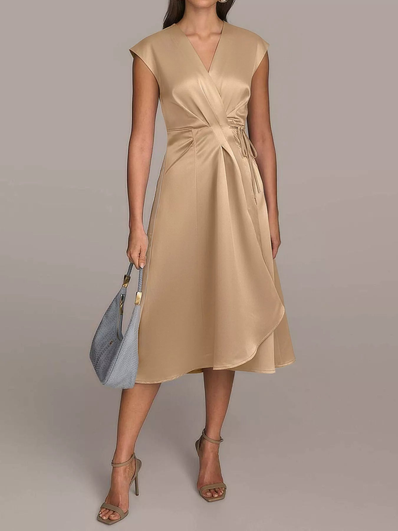 NEWYORKLISTED RUNWAY STYLE: Woman wearing a beige dress holding a blue handbag on a plain background