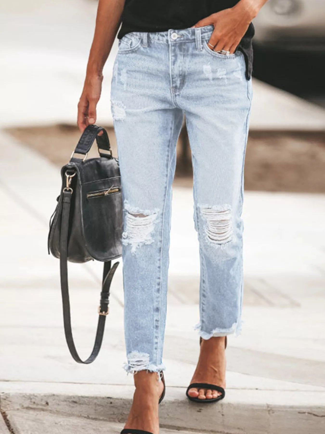 NEWYORKLISTED STYLE COLLECTION: Person wearing light blue distressed jeans holding a black handbag.