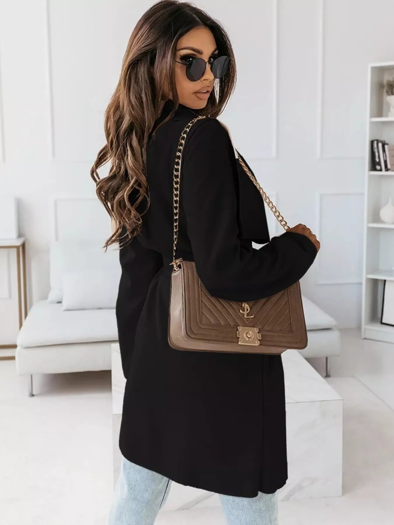 NEWYORKLISTED STYLE COLLECTION: Woman holding a brown handbag with gold chain strap in a modern interior setting