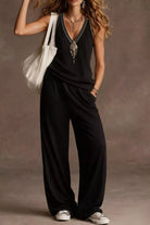 NEWYORKLISTED STYLE COLLECTION: Woman wearing a black jumpsuit with a white bag against a brown background