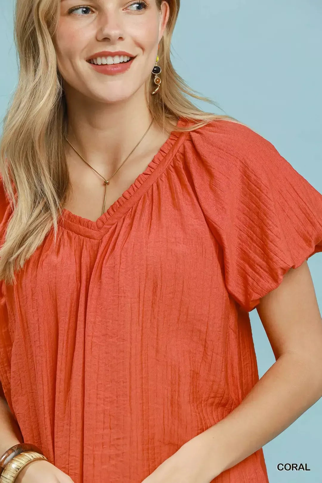 NEWYORKLISTED STYLE COLLECTION: Woman wearing a coral blouse against a light blue background