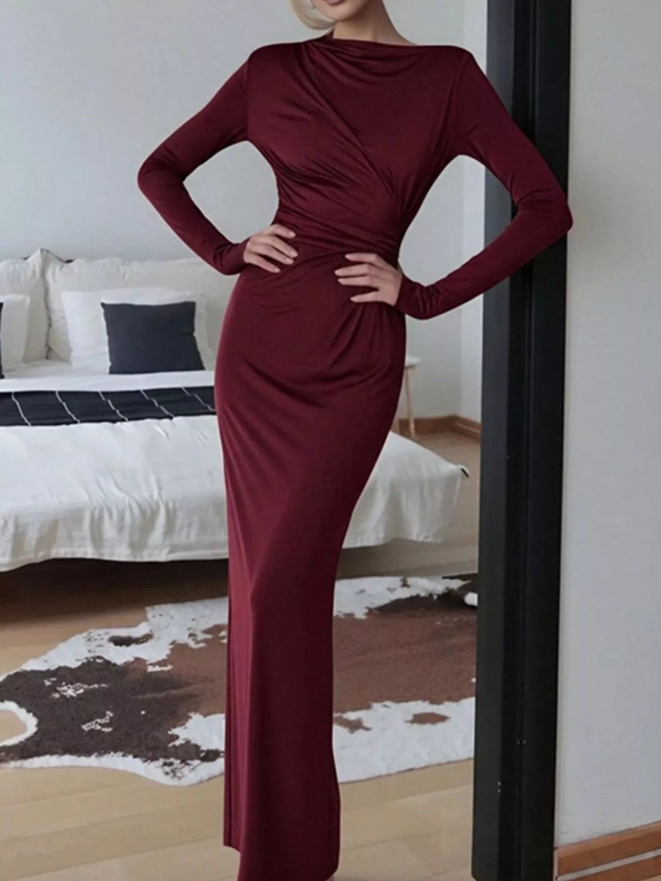 NEWYORKLISTED STYLE COLLECTION: Person wearing a burgundy dress standing in a bedroom.