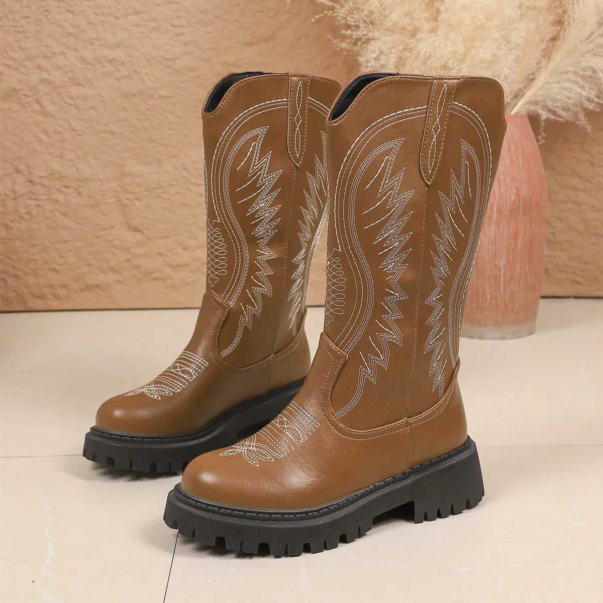 NEWYORKLISTED SHOE COLLECTION: Round Toe Block Heels Boots: Pair of brown cowboy boots with detailed stitching on a beige background
