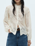 NEWYORKLISTED STYLE COLLECTION: Person wearing a sheer white lace blouse over a black top with blue jeans on a light gray background