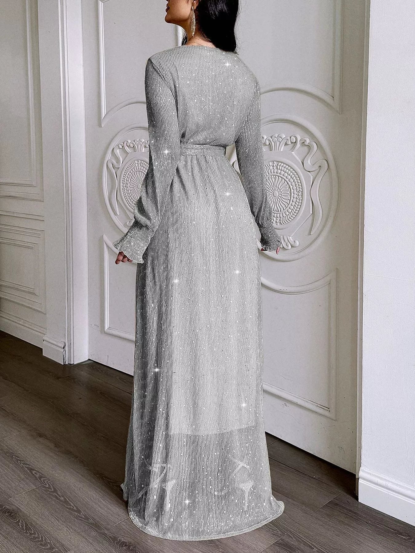 NEWYORKLISTED STYLE COLLECTION: Woman wearing a long, sparkly silver dress in a room with white paneled walls.