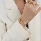 NYLD Glamour Collection by NEWYORKLISTED: Gold heart-shaped bracelet on a person wearing a white blazer.
