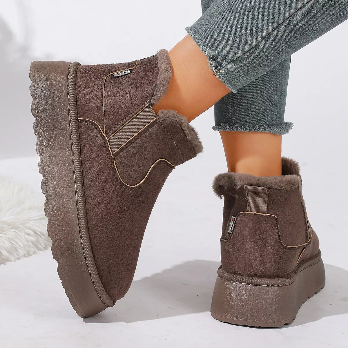 NEWYORKLISTED SHOE COLLECTION: A pair of women's brown suede-look ankle boots with plush faux-fur lining, shown on a model wearing gray frayed-hem jeans against a clean white background.