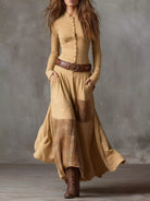 NEWYORKLISTED Style Collection: Woman wearing a long beige dress with plaid accents and brown boots against a gray background