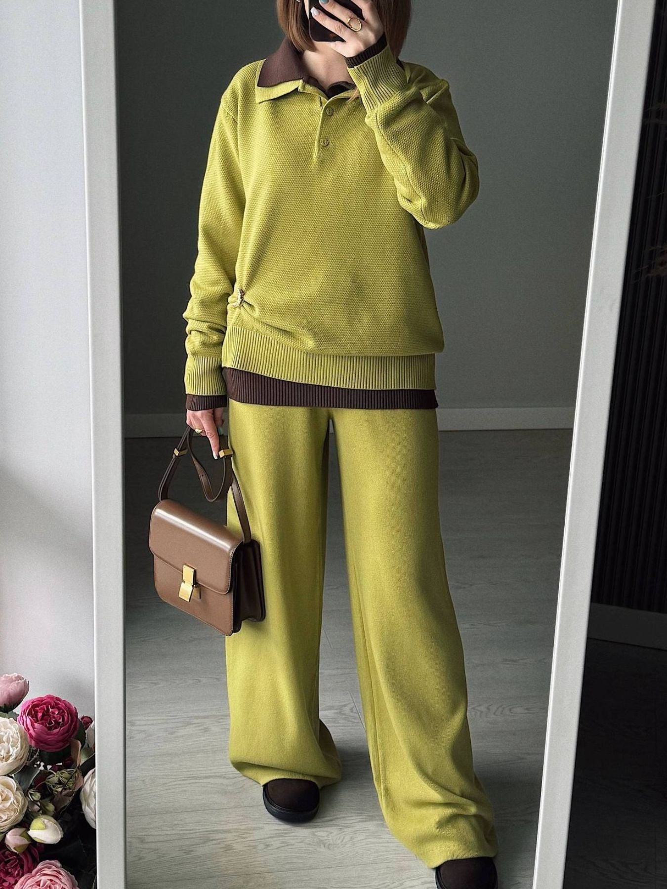 NEWYORKLISTED Comfort Collection: Person wearing a green sweater and pants holding a brown handbag, standing in front of a mirror.