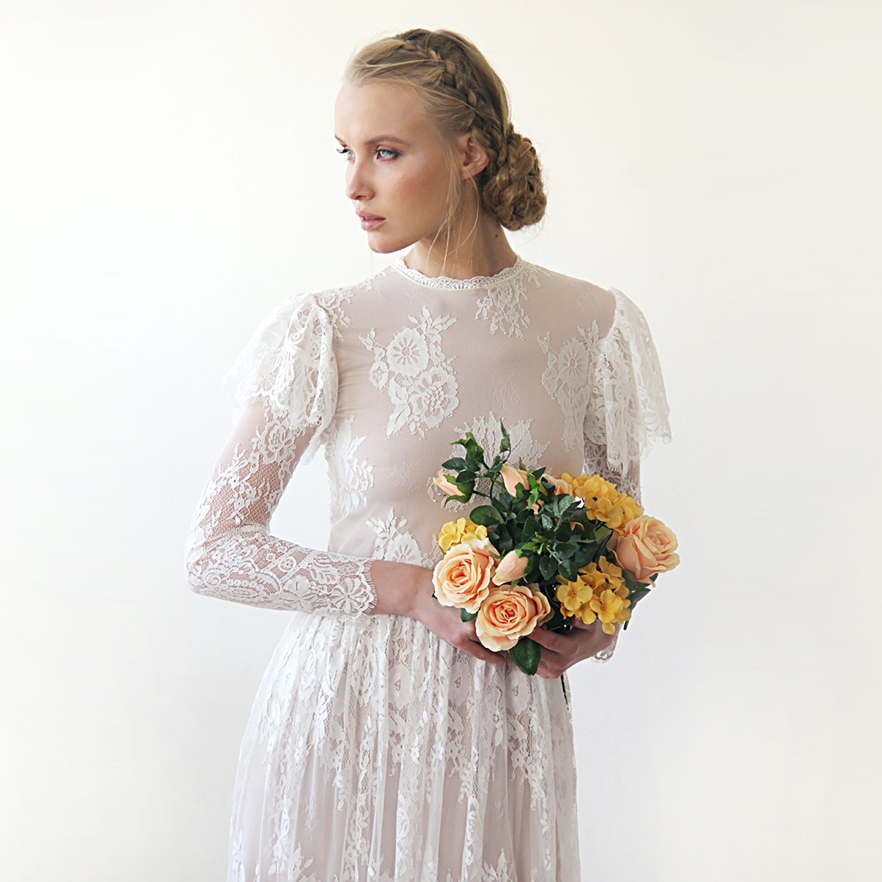 NEWYORKLISTED ELEGANT BRIDE COLLECTION: Woman in a white lace dress holding a bouquet of flowers against a plain background