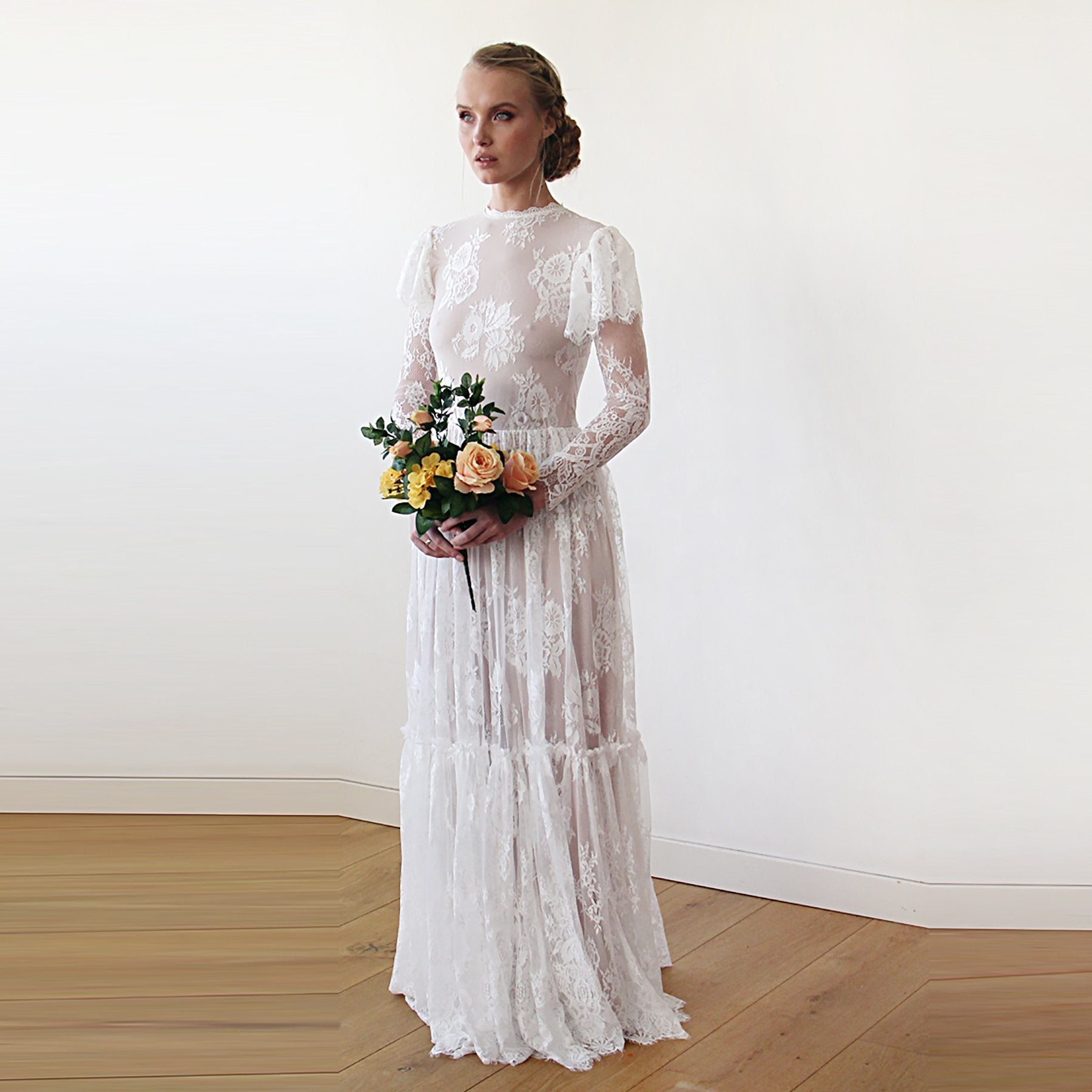 NEWYORKLISTED ELEGANT BRIDE COLLECTION: Woman in a white lace wedding dress holding a bouquet against a plain background