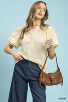 NEWYORKLISTED Style Collection: Woman wearing a cream blouse and blue jeans, holding a brown handbag against a light blue background.