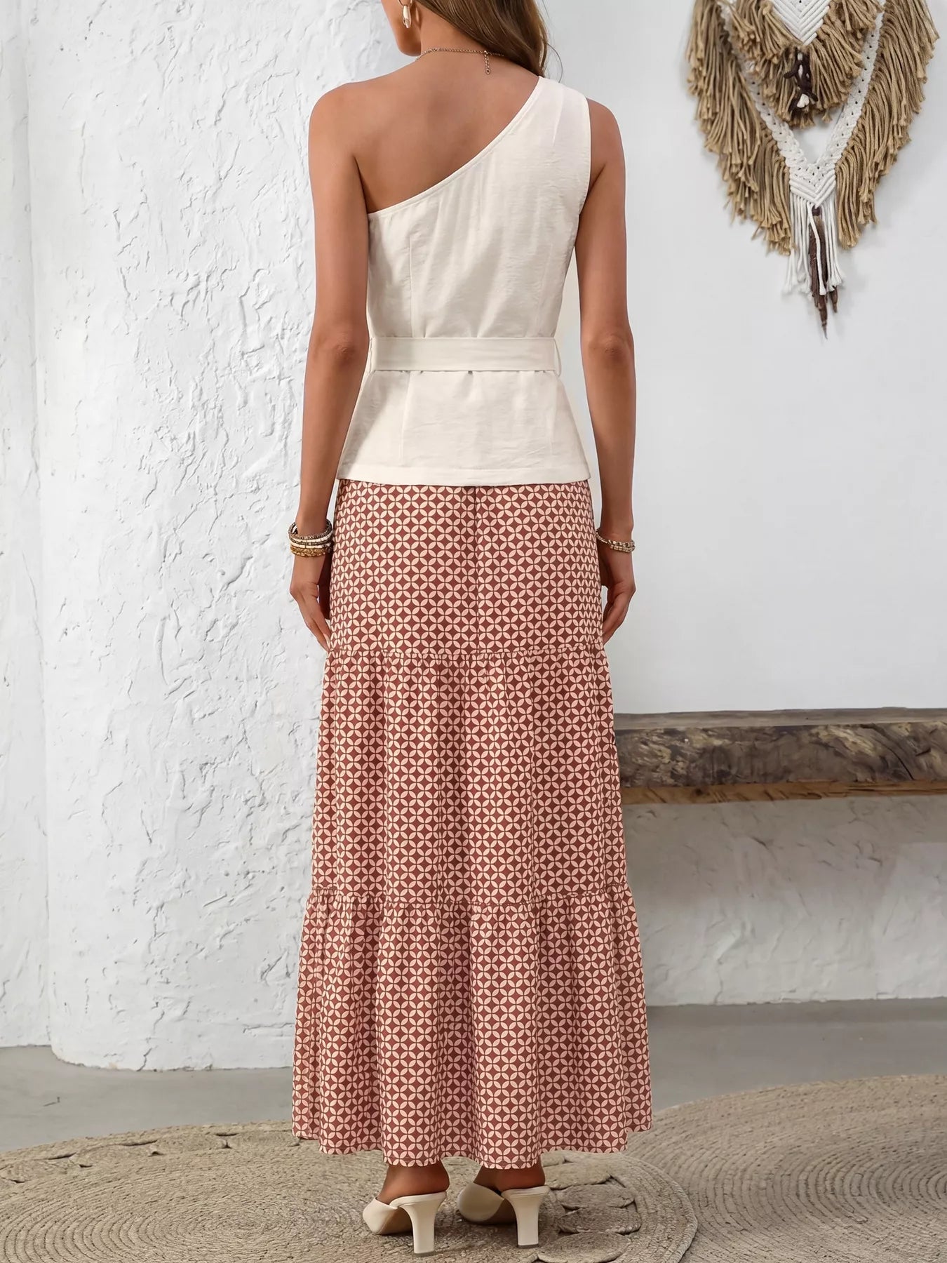 NEWYORKLISTED STYLE COLLECTION: Woman wearing a one-shoulder top and patterned skirt against a white wall.