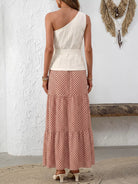 NEWYORKLISTED STYLE COLLECTION: Woman wearing a one-shoulder top and patterned skirt against a white wall.