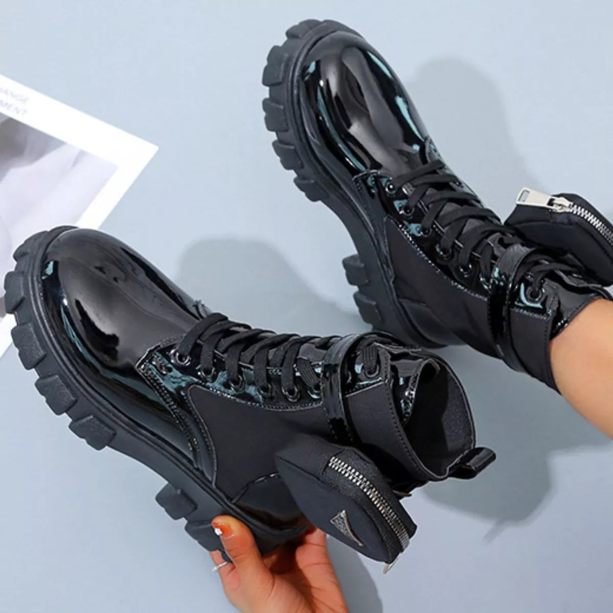 NEWYORKLISTED SHOE COLLECTION: Black high-top sneakers with chunky soles held by a hand on a light blue background