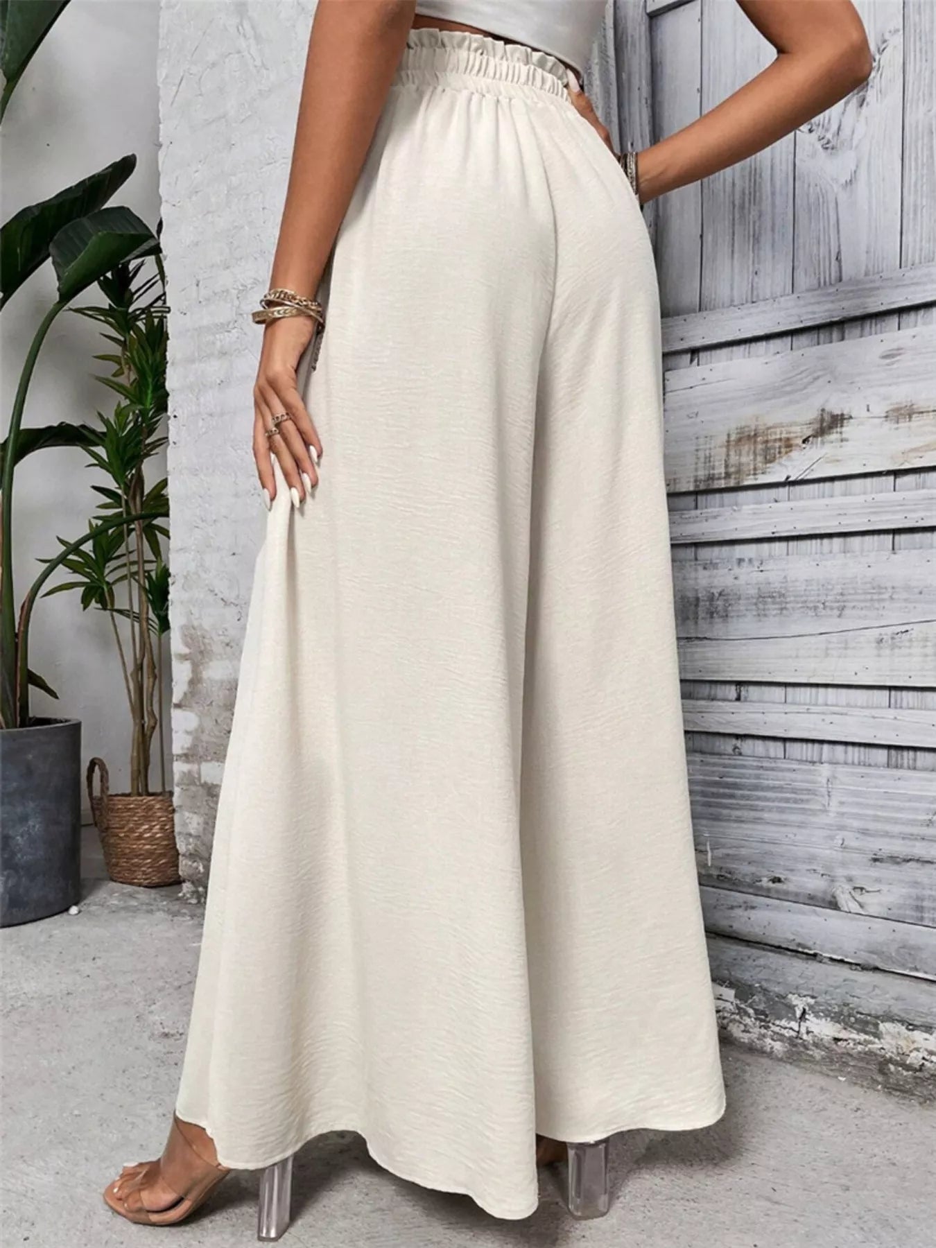 NEWYORKLISTED: Person wearing a long beige skirt standing against a wooden paneled wall.
