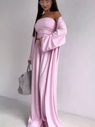 NEWYORKLISTED COMFORT COLLECTION: Woman wearing a pink off-shoulder dress holding a gray handbag against a white background