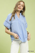 NEWYORKLISTED STYLE COLLECTION: Woman wearing a light blue blouse with white pants on a green background