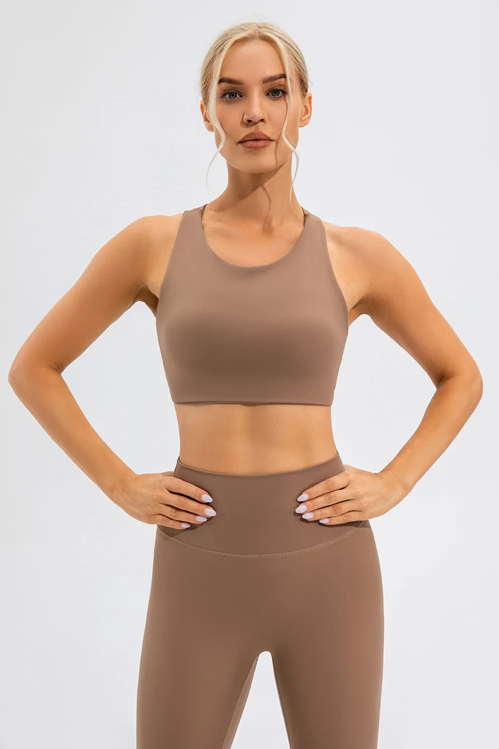 NEWYORKLISTED ACTIVEWEAR COLLECTION: Woman wearing a brown sports bra and leggings on a light gray background