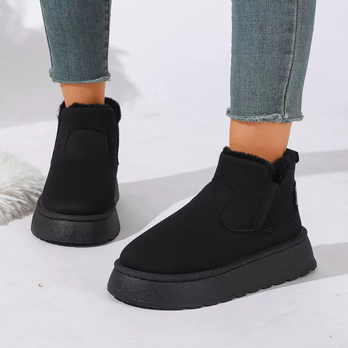 NEWYORKLISTED SHOE COLLECTION: Black platform ankle boots with a fuzzy shearling-style collar, shown on a model wearing blue frayed-hem jeans against a white background.