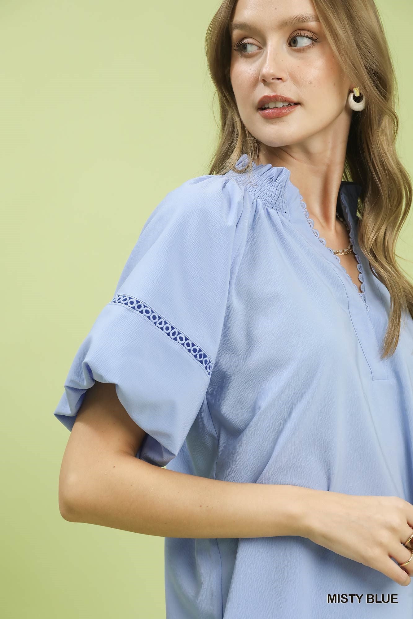 NEWYORKLISTED STYLE COLLECTION: Woman wearing a light blue blouse with embroidered sleeves against a green background