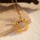 NYLD Glamour Collection by NEWYORKLISTED: Gold crab-shaped pendant with rhinestones on a beige stone surface