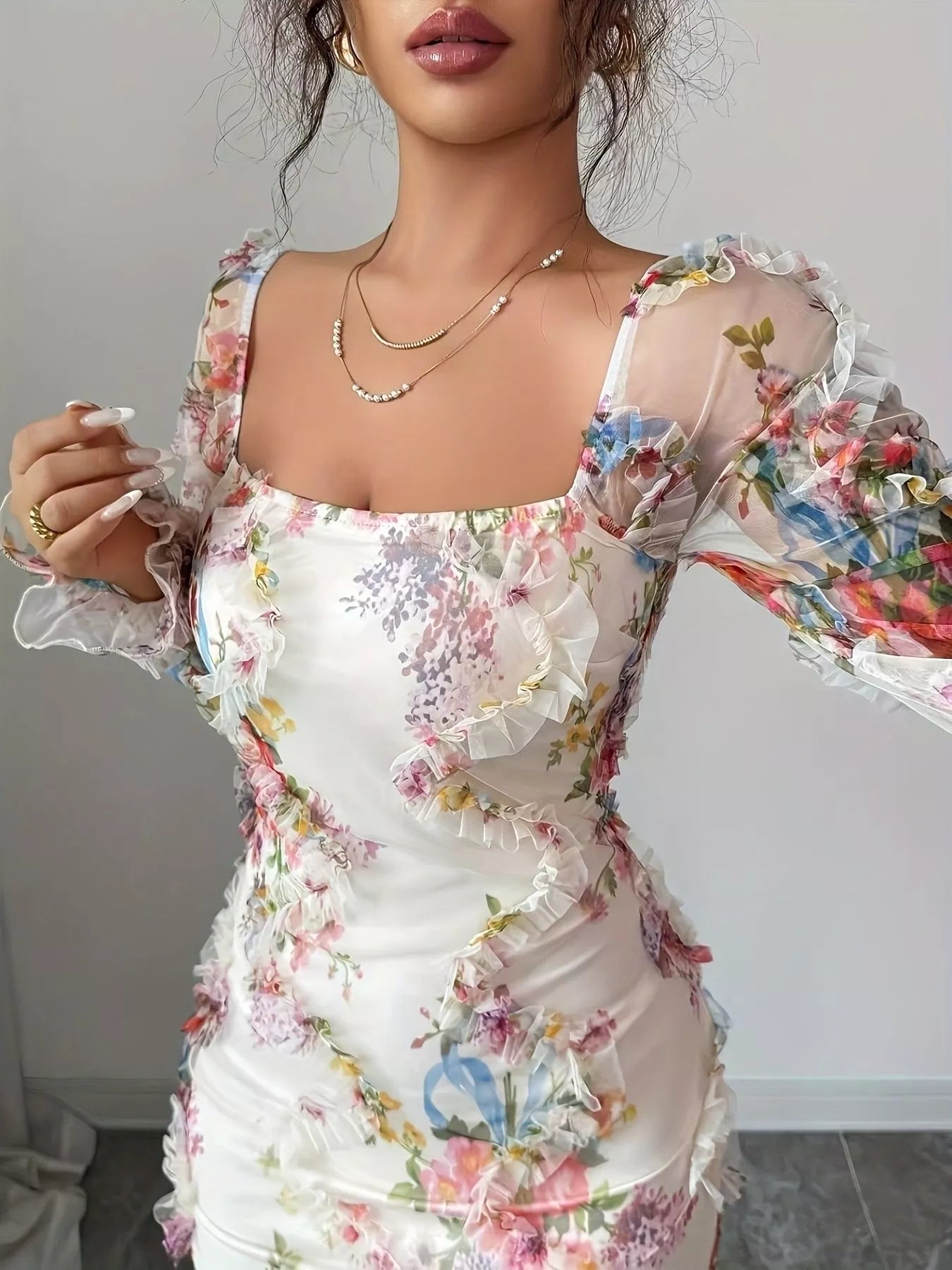NEWYORKLISTED STYLE COLLECTION: Woman wearing a floral dress with sheer sleeves against a neutral background