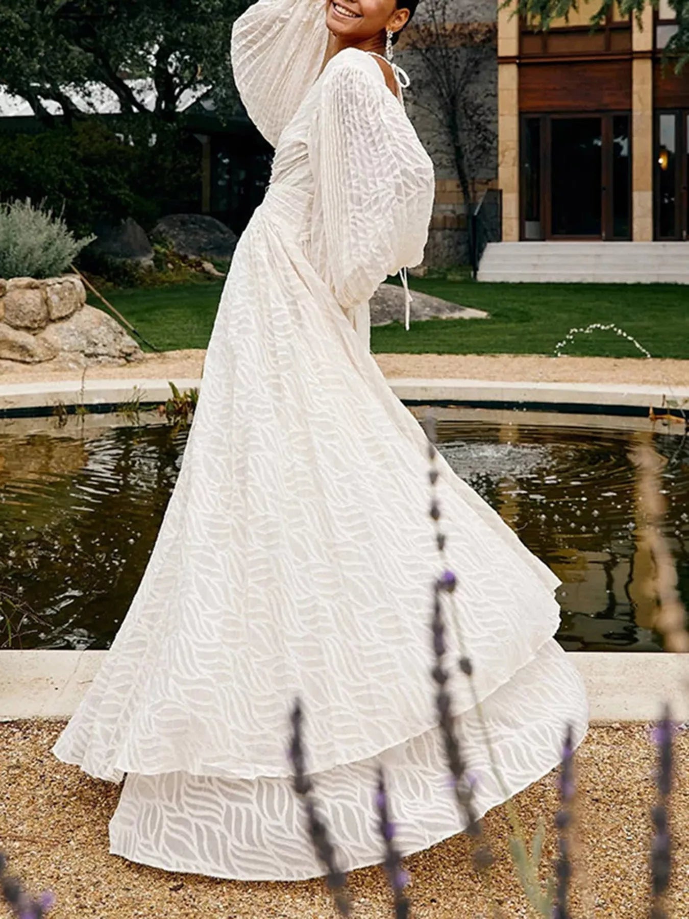 NEWYORKLISTED STYLE COLLECTION: Woman in a white dress standing by a pond with trees and a building in the background
