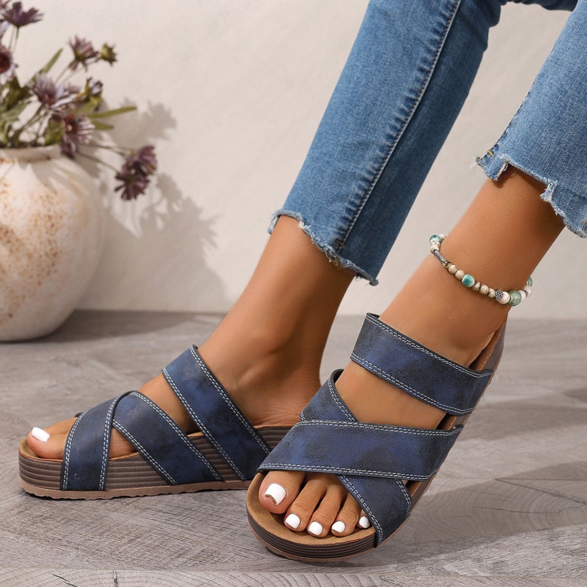 NEWYORKLISTED SHOE COLLECTION: Blue sandals worn with rolled-up jeans on a light wooden floor.