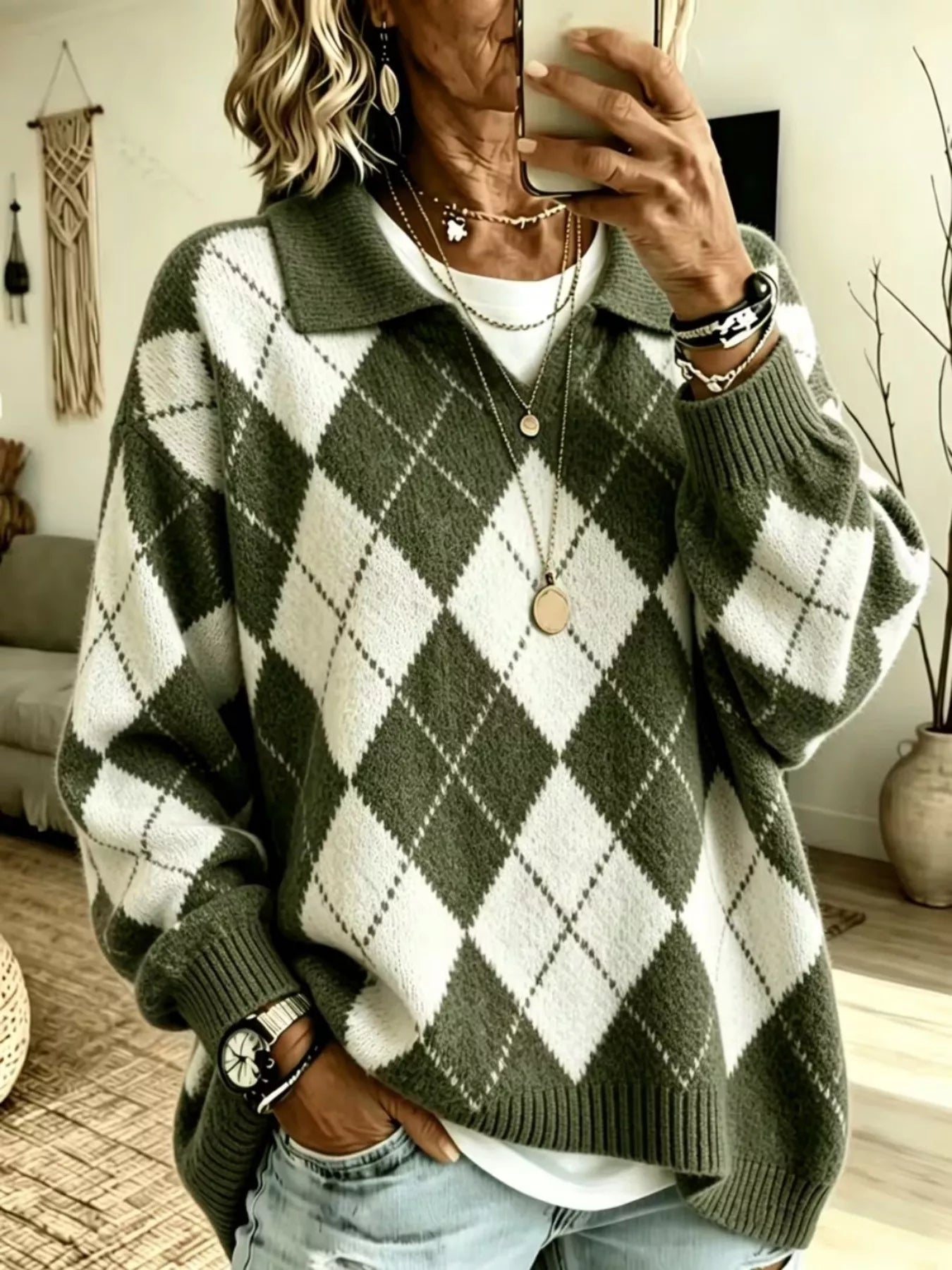 NEWYORKLISTED STYLE COLLECTION: A woman takes a mirror selfie wearing an oversized knit polo sweater with an olive green and white argyle pattern, layered over a white t-shirt and paired with light-wash jeans.