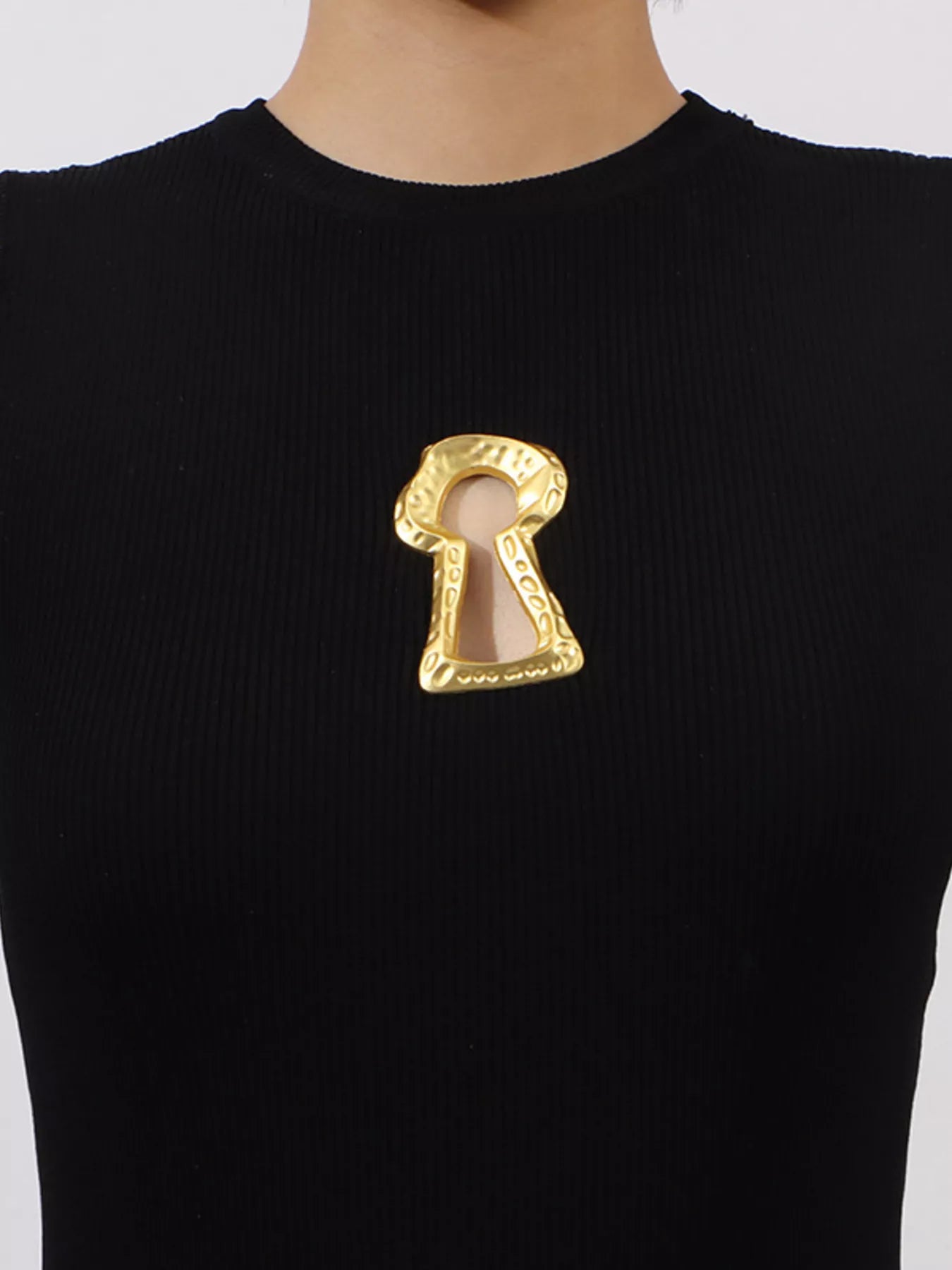 Black sweater with a gold keyhole-shaped brooch on a white background