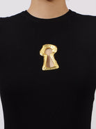 Black sweater with a gold keyhole-shaped brooch on a white background