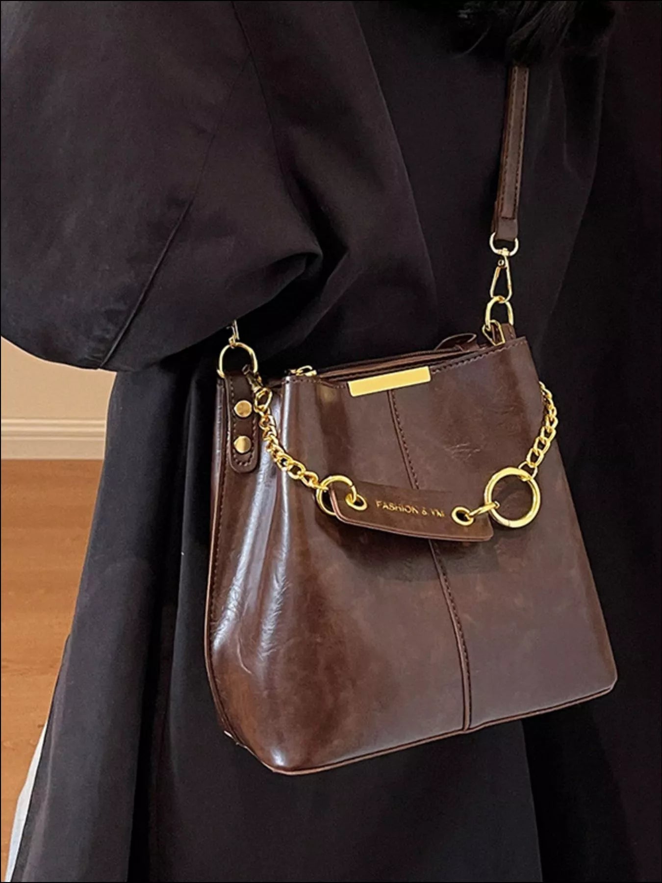 Brown leather handbag with gold chain strap held by a person wearing a dark coat. New York Listed Style Collection 
