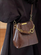 Brown leather handbag with gold chain strap held by a person wearing a dark coat. New York Listed Style Collection 
