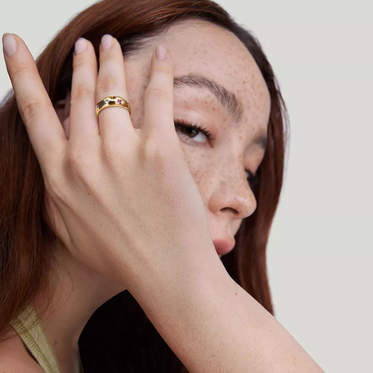 NYLD Glamour Collection by NEWYORKLISTED: Woman with freckles on her face wearing a gold ring, against a plain background