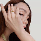 NYLD Glamour Collection by NEWYORKLISTED: Woman with freckles on her face wearing a gold ring, against a plain background