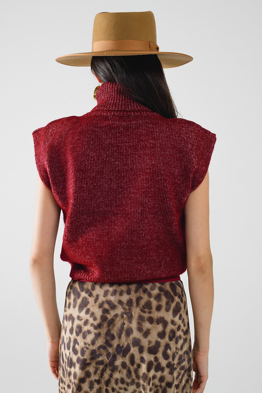 Person wearing a red sleeveless sweater and leopard print skirt with a beige hat on a white background