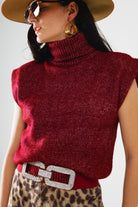 Woman wearing a red sleeveless knitted top with a belt, sunglasses, and a hat on a light gray background