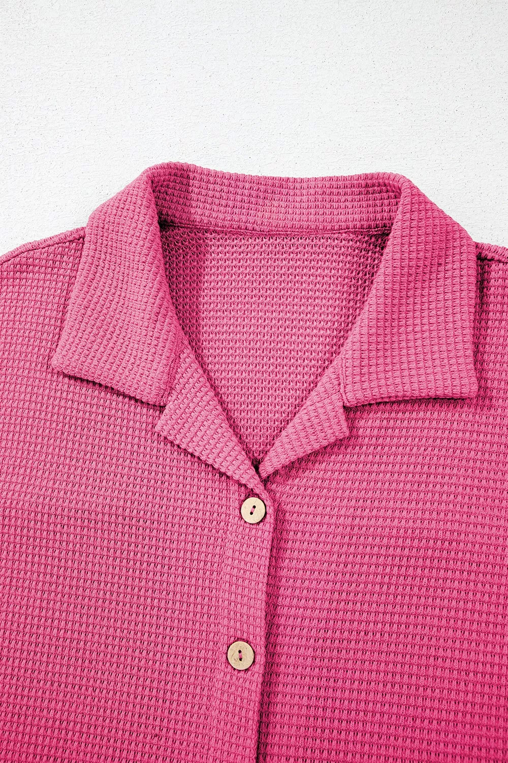 NEWYORKLISTED Comfort Collection: Close-up of a pink textured polo shirt with buttons on a light gray background