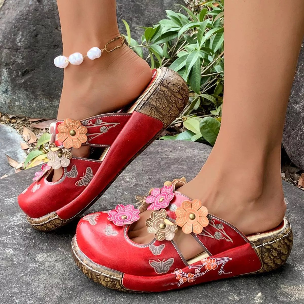 NEWYORKLISTED SHOE COLLECTION: Red floral embellished shoes worn on a stone surface with greenery in the background
