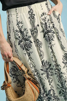 NEWYORKLISTED STYLE COLLECTION: Person wearing a patterned skirt holding a straw bag against a blue background