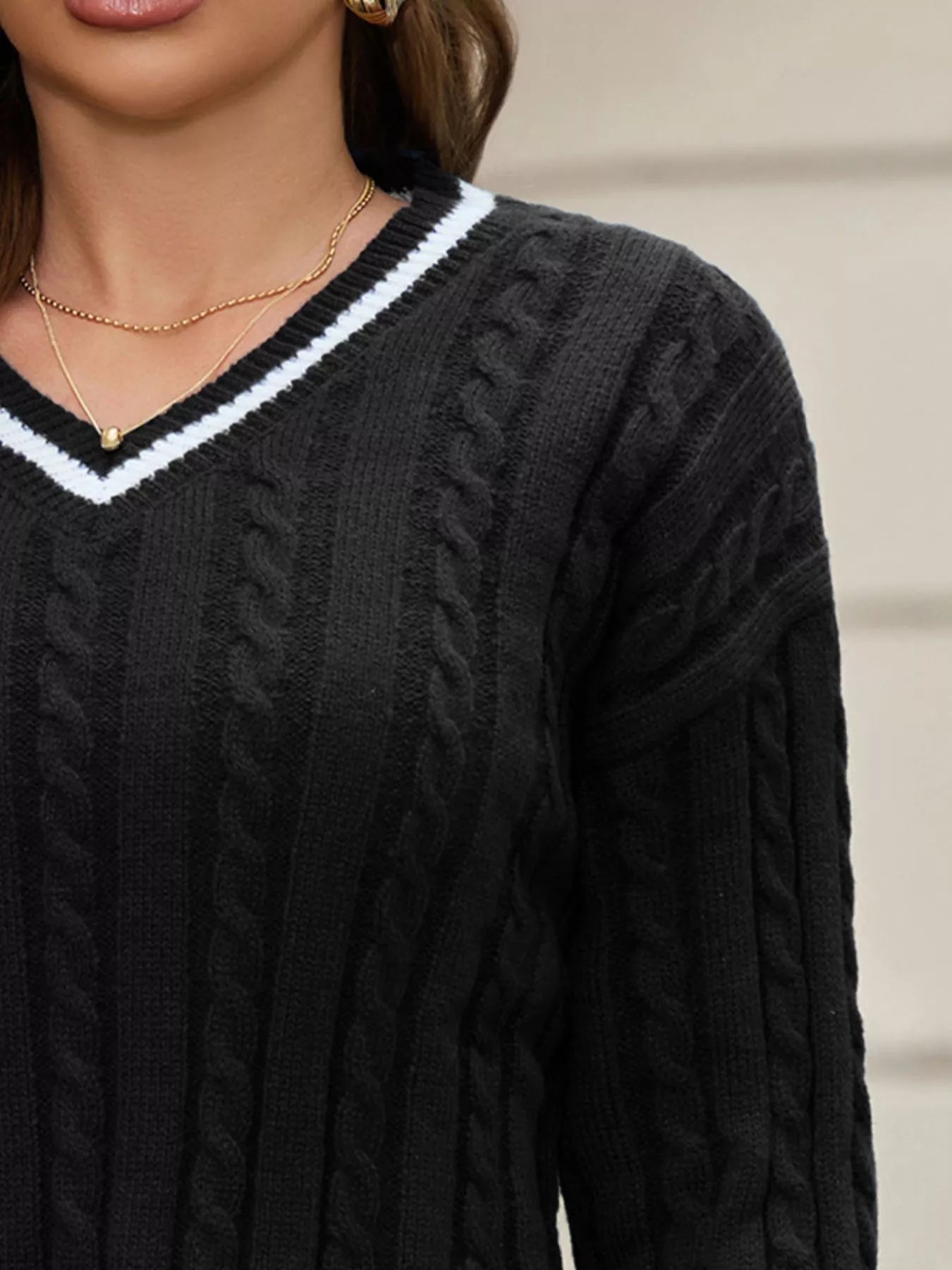 NEWYORKLSITED STYLE COLLECTION: Black cable knit sweater with white trim worn by a person.