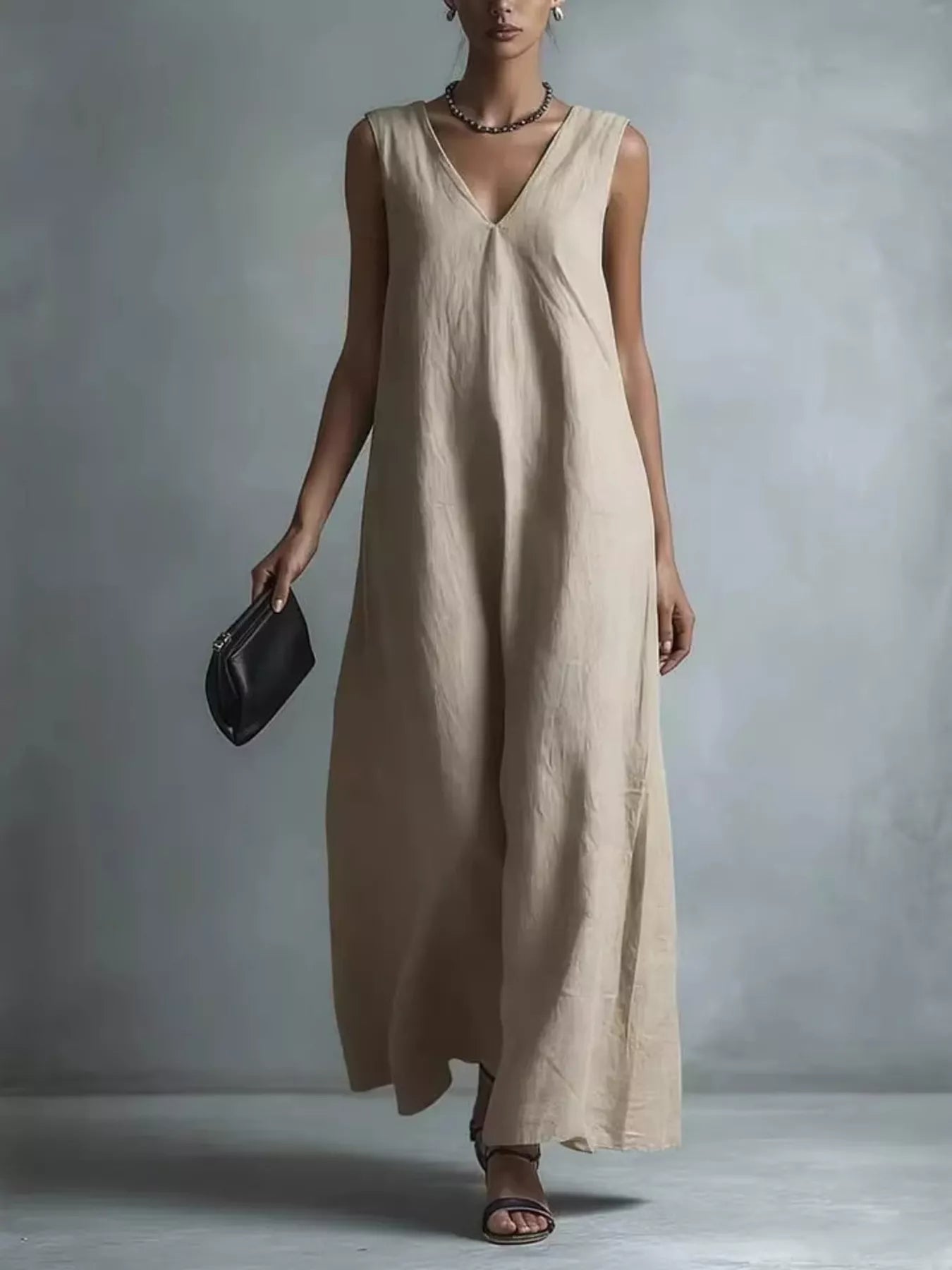 NEWYORKLISTED STYLE COLLECTION: A woman models a sleeveless, V-neck maxi dress in a light beige linen-like fabric, holding a small black clutch against a textured gray studio background.