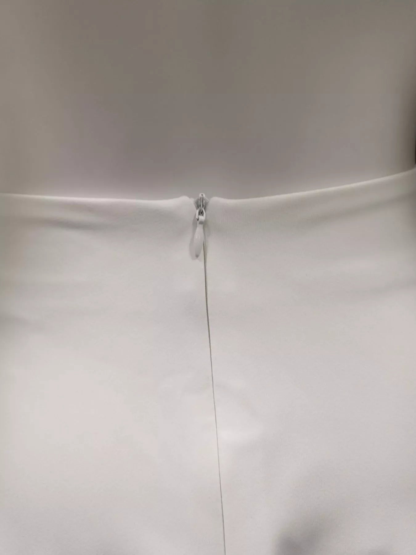 NEWYORKLISTED STYLE COLLECTION: Close-up of a white dress with a zipper on a plain background