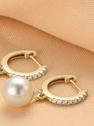 NYLD GLAMOUR COLLECTION by NEWYORKLISTED: Gold hoop earrings with a pearl and small diamonds on a beige fabric background